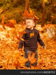 Picture of cute little boy enjoying autumnal nature, pretty infant playing in park, little child playing with old dry trees foliage, adorable toddler play game on backyard, happiness concept&#xA;