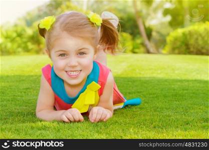 Picture of cute little girl lying down on green grass in park, cheerful child resting on the field on backyard, pretty kid having fun outdoors in springtime, spring nature, sunny day, happy childhood