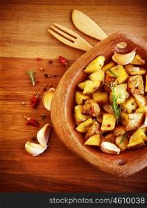 Picture of fried potato with garlic and spices on wooden table, baked quartered potato with vegetables serve in wooden plate with knife and fork, homemade french fries, restaurant dish