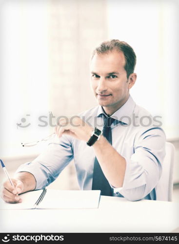 picture of handsome businessman with spectacles writing in notebook
