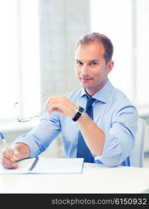 picture of handsome businessman with spectacles writing in notebook. businessman with spectacles writing in notebook