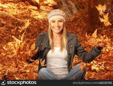 Picture of happy blonde girl having fun in autumn woods, pretty woman throwing up dry autumnal leaves in the forest, beautiful female sitting down on ground covered golden foliage&#xA;&#xA;&#xA;