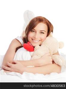 Picture of happy woman laying down in the bed, girl enjoying romantic present, soft bear and red handmade heart-shape toy as gift for Valentines day holiday, isolated on white background, love concept