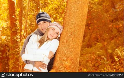 Picture of loving couple standing and hugging near tree in autumnal forest, romantic relationship, leisure time, fall season, autumn vacation, enjoying nature, love concept