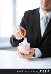picture of man putting coin into small piggy bank