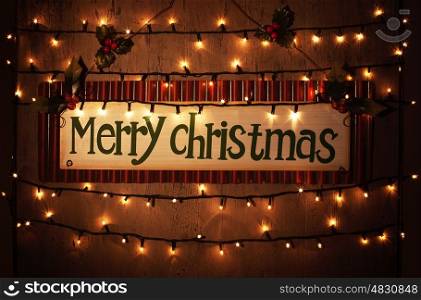 Picture of Merry Christmas banner on brown grunge door at home, happy New Year, glowing electrical garland, Christmastime house interior, congratulations postcard, holiday illumination