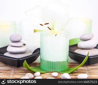 Picture of pebble stones in black plate, white lily flower, fresh green leaves, candle on wooden table in spa salon, aroma therapy, zen balance, luxury spa resort, natural cosmetic, relaxation concept