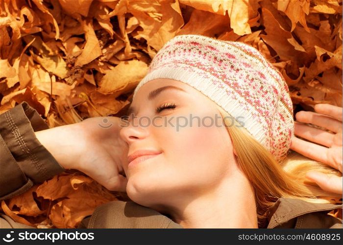 Picture of pretty woman sleeping outdoors, cute female laying down on autumnal foliage with closed eyes, pleasure expression on face of young woman, autumn park, leisure time, joy concept