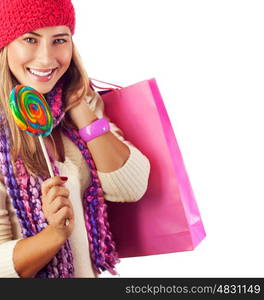 Picture of pretty woman with colorful bonbon and pink present bag isolated on white background, happy woman holding shopping bag and lick sweet candy, red warm hat, Christmas sale, New Year gift