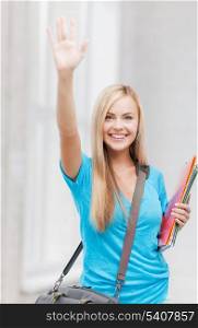 picture of smiling student with folders waving her hand
