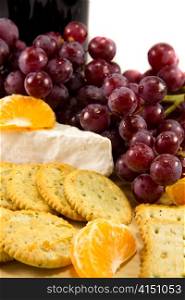 Picture of some grapes brie and some clementins with a bottle of red wine in the background
