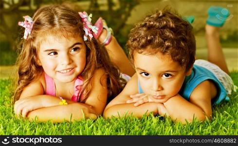 Picture of two happy kids laying down on fresh green grass, brother and sister enjoying summer holiday, cute girl and pretty boy having fun outdoors, happy friends playing on backyard&#xA;