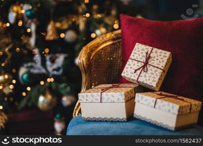 Picture of wrapped gift boxes lie on armchair against decorated New Year tree background. Preperation for holiday. Beautiful Christmas tree with garlands and presents indoors