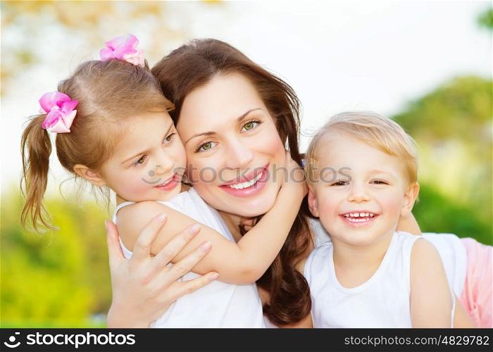 Picture of young mother hugging two little children, closeup portrait of happy family, cute brunette female with daughter and son outdoor in spring time, smiling faces, happiness and love concept