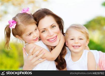 Picture of young mother hugging two little children, closeup portrait of happy family, cute brunette female with daughter and son outdoor in spring time, smiling faces, happiness and love concept