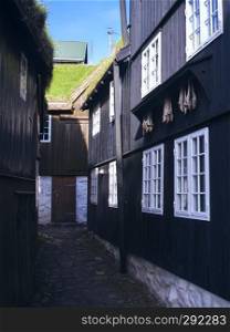 Picturesque black-tarred grass-roofed houses with dried fish hanging on hooks and narrow cobblestone street in Torshavn, the Captivating Capital of the Faroe islands on Island Streymoy. Postcard motif.
