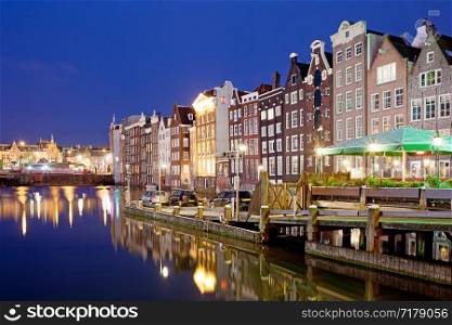 Picturesque city of Amsterdam in Holland, Netherlands at night with historic Dutch style row houses by the canal.