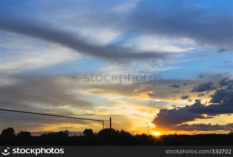 Picturesque clouds in the summer sunset sky over silhouettes of trees and beach volleyball net. Selective focus.