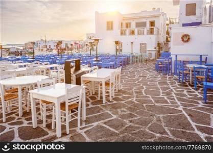 Picturesque narrow street with traditional whitewashed houses with cafe tables of Naousa town in famous tourist attraction Paros island, Greece on sunrise. Picturesque Naousa town street on Paros island, Greece