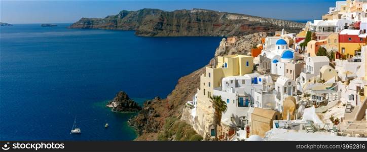 Picturesque panorama of Oia or Ia on the island Santorini, white houses, windmills and church with blue domes, and island Therasia, Greece