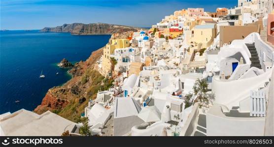 Picturesque panorama of Oia or Ia on the island Santorini, white houses, windmills and church with blue domes, and island Therasia, Greece