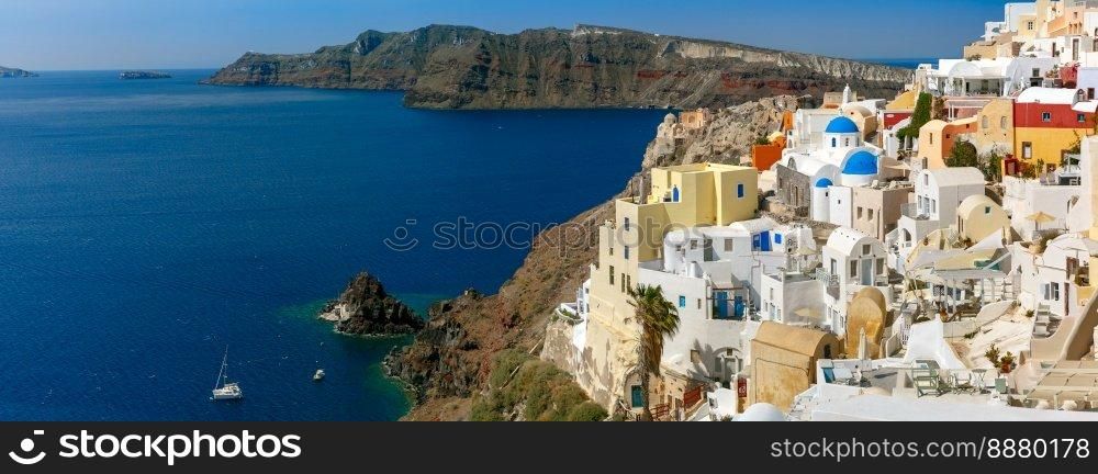 Picturesque panorama of Oia or Ia on the island Santorini, white houses, windmills and church with blue domes, and island Therasia, Greece. Panorama of islands Santorini and Therasia, Greece