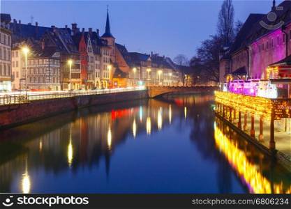 Picturesque quay and church of Saint Nicolas with mirror reflections in the river Ile and Christmas garland during morning blue hour, Strasbourg, Alsace, France