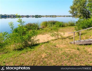 Picturesque summer evening sunset lake calm beach with camping pitch on shore and wooden stairs to the water. Concept of tranquil country life, eco friendly tourism, camping, fishing.