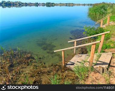 Picturesque summer lake calm beach with wooden stairs to the water. Concept of tranquil country life, eco friendly tourism, camping, fishing.