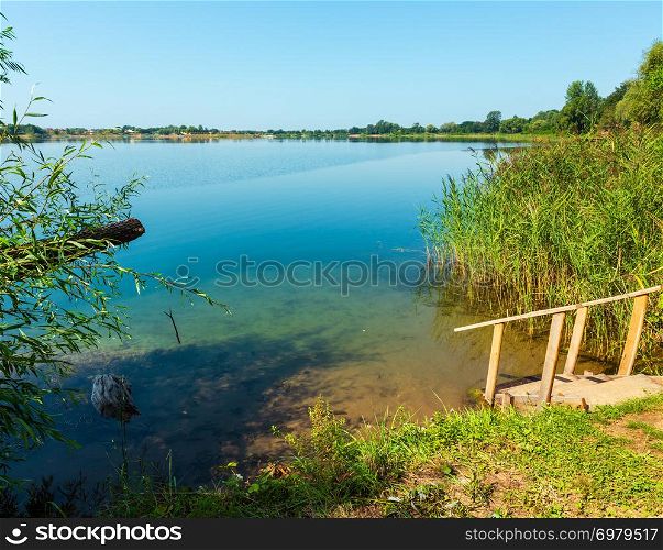 Picturesque summer lake calm beach with wooden stairs to the water. Concept of tranquil country life, eco friendly tourism, camping, fishing.