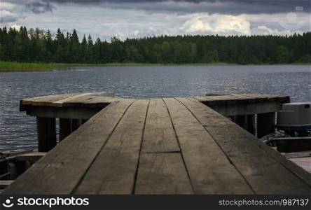 Picturesque view from a wooden pier on a forest lake in windy cloudy weather. Atmospheric landscape with space for copy, selective focus. Seliger Lake, Russia.
