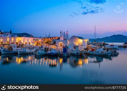 Picturesque view of Naousa town in famous tourist attraction Paros island, Greece with traditional whitewashed houses and moored fishing boats and seaside restaurants and cafe illuminated in night. Picturesque Naousa town on Paros island, Greece in the night