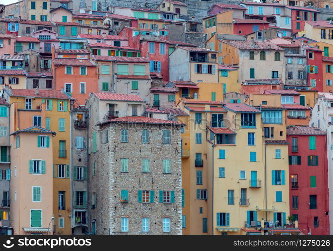 Picturesque view of the multicolored medieval houses in the historic part of the city. Menton. France.. Menton. Antique multi-colored facades of medieval houses on the shore of the bay.