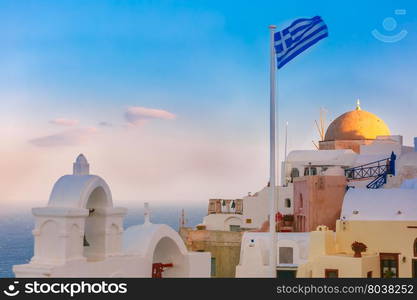 Picturesque view of white houses, church and Greek flag in the morning, Oia or Ia, island Santorini, Greece