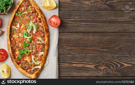 Pide is a Turkish boat-shaped flatbread stuffed with minced lamb and beef, with spices and herbs. Wooden table, top view, flat lay, copy space