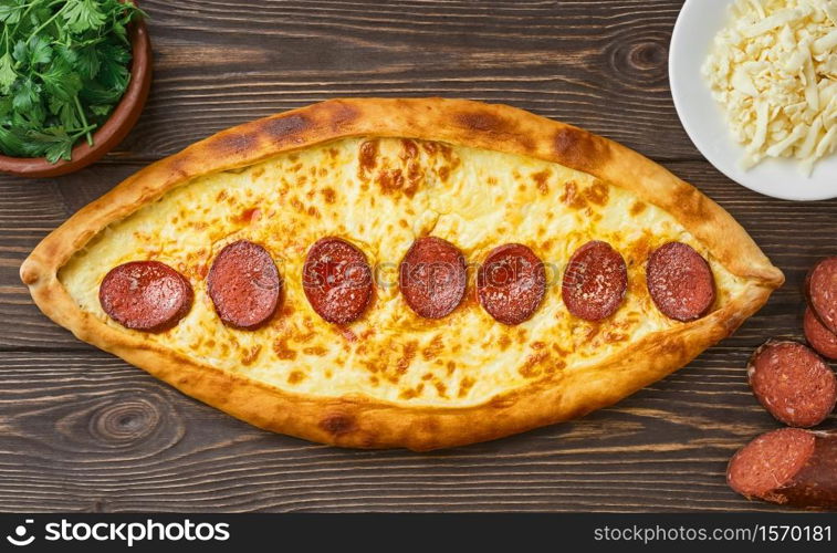 Pide - Turkish boat-shaped flatbread with sausage (sudjuk) with spices and herbs. Wooden dark table, top view, flat lay