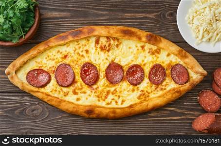 Pide - Turkish boat-shaped flatbread with sausage (sudjuk) with spices and herbs. Wooden dark table, top view, flat lay