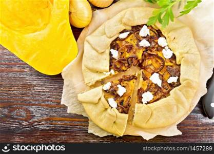 Pie of pumpkin, fried onions and soft cheese on parchment, napkin, parsley on a wooden board background from above