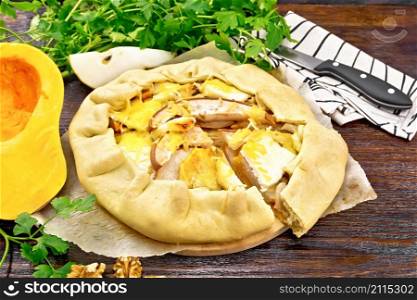 Pie of pumpkin, pear, soft cheese and walnuts on parchment, napkin and knife, parsley on a wooden board background
