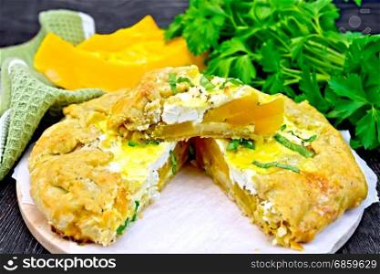 Pie of pumpkin, salty feta cheese, egg, cream and herbs, green napkin, basil and parsley on a background of wooden boards