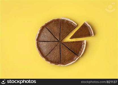 Pie slice separated from the whole pumpkin pie on yellow background. Minimal flat lay of autumn dessert. Traditional homemade American pie.
