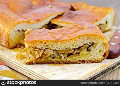 Pie with cabbage and chanterelles, knife, napkin against a wooden board