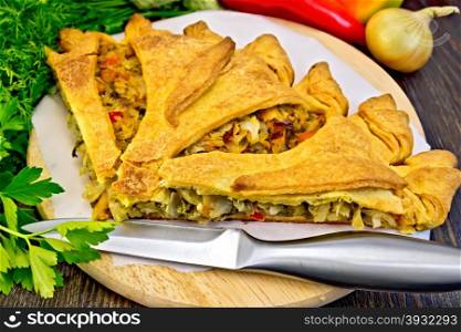 Pie with cabbage, sorrel and sweet pepper, knife, onion, parsley on a wooden boards background