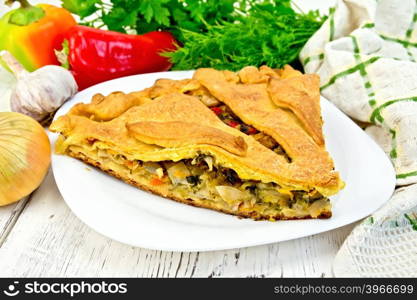 Pie with cabbage, sorrel and sweet peppers in a white plate, napkin, parsley on the background light wooden boards