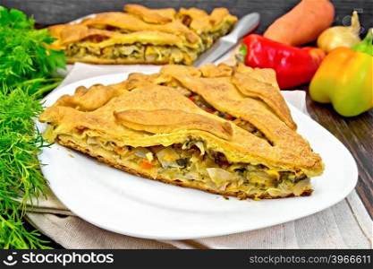 Pie with cabbage, sorrel and sweet peppers in a white plate on a napkin, parsley and vegetables on the background of wooden boards