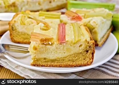 Pie with curd and rhubarb, fork in a plate on a napkin, rhubarb stalks on the background of wooden boards