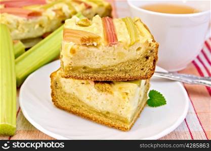 Pie with curd and rhubarb, fork on the plate, a mug of tea, rhubarb stalks on a background of linen napkins