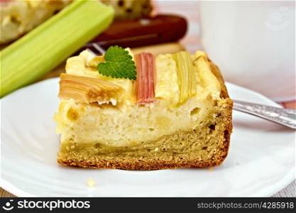 Pie with curd and rhubarb, fork on the plate, a mug of tea, rhubarb stalks on a background of linen napkins