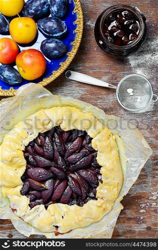 Pie with plums. Rustic pie with plums and plum jam on wooden background