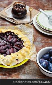 Pie with plums. Rustic pie with plums and plum jam on wooden background